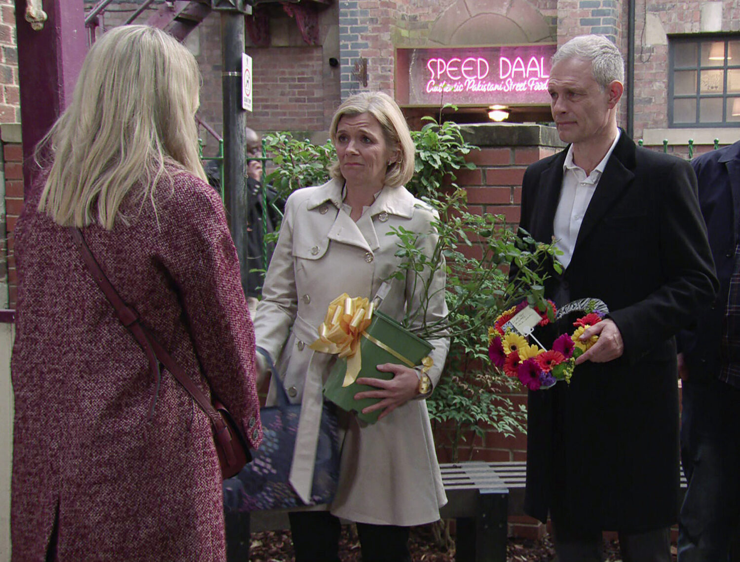 Leanne and Nick are holding plants whilst speaking to Toyah on Coronation Street